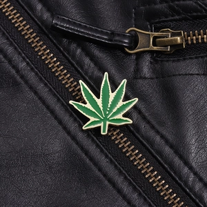 Macro detail of a green maple leaf enamel pin on a black leather jacket with gold edges