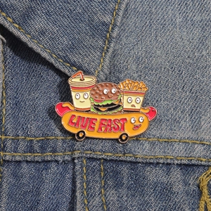 Detail of cartoon fast food enamel pin with Live Fast text on blue denim jacket
