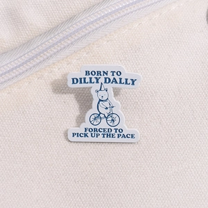 Close-up of bear riding a bicycle enamel pin on a white canvas bag texture