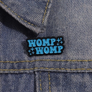 Dettaglio di una spilla smaltata blu WOMP WOMP sul colletto di una giacca denim