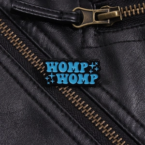 Dettaglio della spilla smaltata blu WOMP WOMP su giacca di pelle nera con zip