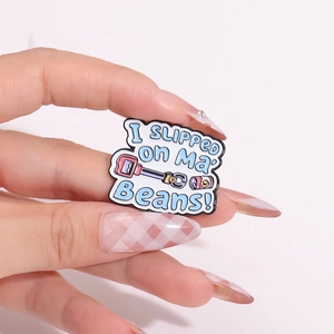 Enamel pin with I Slipped on My Beans text and pink can illustration on hand