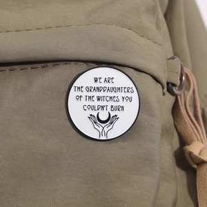 Close-up of a white enamel feminist badge pinned on a green canvas bag showing a moon graphic