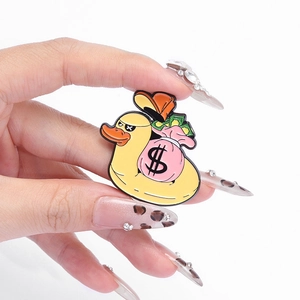Cartoon enamel duck pin with money bag and dollar sign badge held by a hand