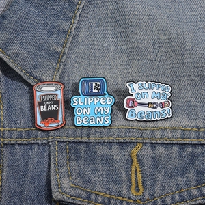 Three-piece funny enamel pins with 'I SLIPPED ON MY BEANS' quotes on blue denim jacket
