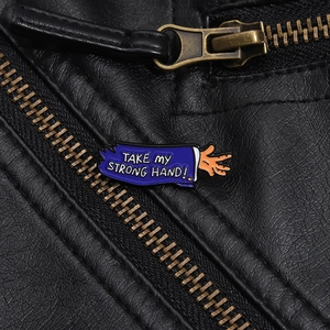 Détail macro du badge émaillé 'Take My Strong Hand' sur une veste en cuir noir