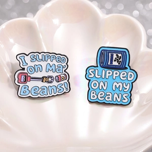 Blue and white enamel bean quote brooches displayed on a decorative ceramic shell plate