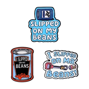 Cartoon enamel pin set with 'I Slipped On My Beans' slogan on a white background