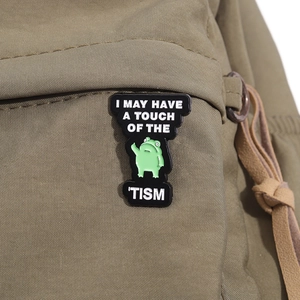 Funny green frog enamel pin with I May Have A Touch Of The Tism text on fabric