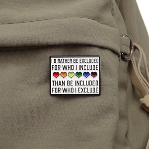 Detail of enamel pin with rainbow hearts and inclusive text on olive canvas fabric