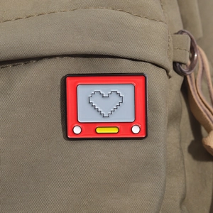 Makroaufnahme einer roten Retro-TV Emaille-Anstecknadel mit Pixelherz auf Rucksack