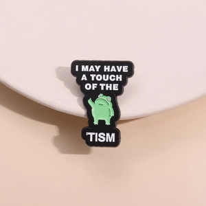Cartoon frog enamel pin with I May Have A Touch Of The Tism text on beige background