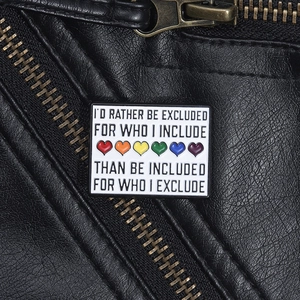 Rectangular enamel pin with rainbow hearts and social inclusion quote on leather jacket