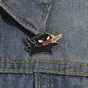 Creative black enamel cat pin holding a knife with CRIME text on blue denim fabric