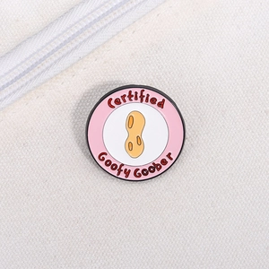Detail of round pink enamel pin featuring a peanut and Certified Goofy Goober text