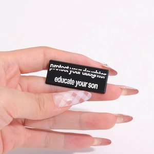 Schwarze Emaille-Brosche mit Textaufdruck 'protect your daughter' von Hand gehalten