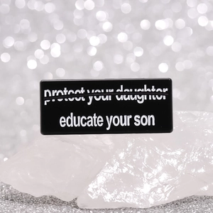 Black rectangular enamel pin with educate your son slogan on white crystal stones