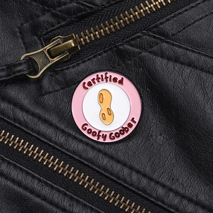 Close-up of a Goofy Goober peanut enamel pin on a black leather jacket with metal zipper