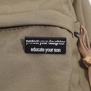 Nahaufnahme von schwarzen Emaille-Pins mit Slogans auf olivgrünem Rucksack