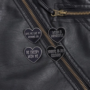 Detail of four black heart enamel pins with punk quotes on black leather texture