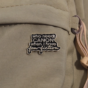 Détail du pin's en émail sur sac en toile avec le texte who needs CANON when i have fan-fiction