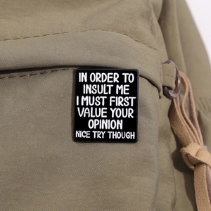 Detail of black rectangular enamel pin with white quote on a khaki fabric backpack