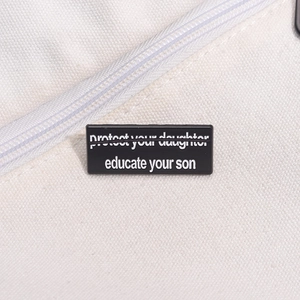 Close-up of black enamel badge with Educate Your Son text on a beige canvas background