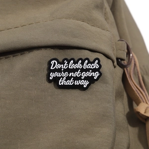 Detail of enamel badge with motivational quote on green canvas backpack