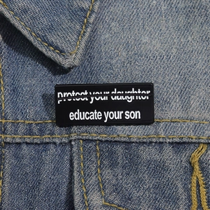 Nahaufnahme der schwarzen Emaille-Anstecknadel mit Text auf einer blauen Jeansjacke
