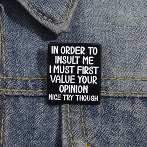 Detail of rectangular black enamel pin with white text on a blue denim jacket pocket