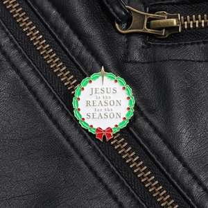 Détail de la broche couronne de Noël émaillée avec phrase festive sur veste en cuir noir