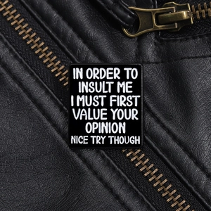 Close-up of black enamel slogan pin featuring bold text on a leather jacket lapel