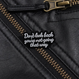 Close-up of geometric enamel brooch on black leather with inspirational English text
