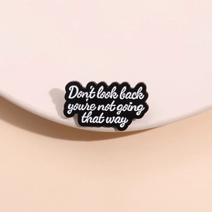 Black enamel wave brooch with Don't Look Back quote on a white minimalist pedestal