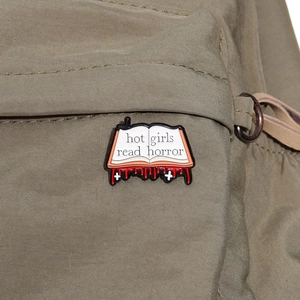 Halloween horror book enamel pin badge featuring Hot Girls Read Horror on army green bag