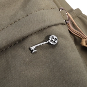 Détail d'une broche clé vintage en métal argenté sur un tissu texturé de couleur vert olive