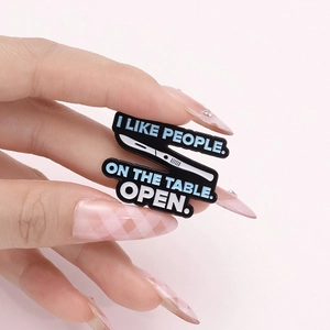 Funny enamel lapel pin with black surgical knife design and humorous medical quote