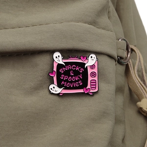 Pink retro TV enamel pin with spooky movies text on a green canvas backpack