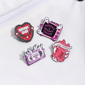 Detail of horror themed enamel pins with Halloween ghost and retro TV motifs on white canvas