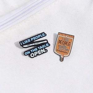 Detail of medical humor enamel pins featuring a black scalpel and orange IV bag on canvas
