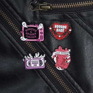 Detail of horror-themed enamel pins featuring heart and TV motifs on a black leather jacket