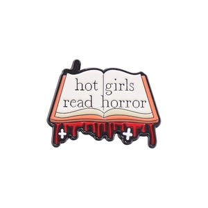 Gothic enamel pin featuring an open book design with Hot Girls Read Horror slogan