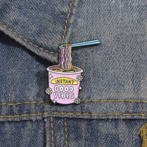 Close-up of noodle enamel pin with Instant Good Vibes text on blue denim jacket