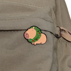 Detail of Christmas capybara enamel pin with festive wreath on an olive green canvas bag