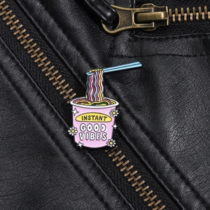 Detail der Emaille-Anstecknadel mit rosa Nudeltopf und Regenbogen-Nudeln auf Leder