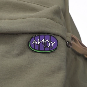 Detailed macro shot of an oval Andy enamel pin attached to a green nylon fabric strap