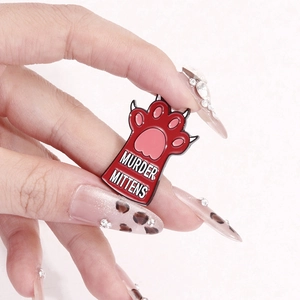 Red cat paw enamel pin with Murder Mittens text in creative hand-held display