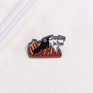 Close-up of black bird fire enamel pin featuring Everything Is Fine text on white canvas