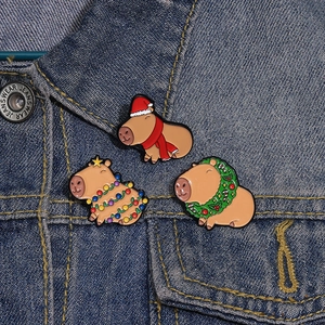 Three cute Christmas Capybara enamel pins with Santa hat and wreath on denim jacket