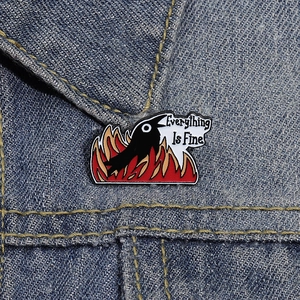 Funny crow in flames enamel pin with Everything Is Fine text on denim jacket